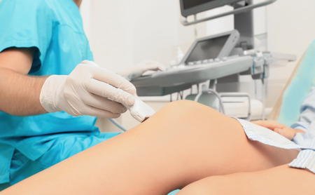 Doctor conducting ultrasound examination of patient's knee in clinicの写真素材