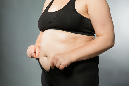 Overweight woman in tight pants on grey background. Weight loss conceptの写真素材