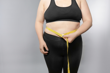 Overweight young woman measuring her belly on grey background. Weight loss conceptの写真素材