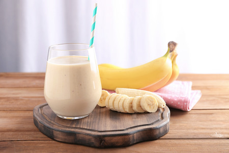 Glass with delicious banana smoothie on wooden boardの写真素材
