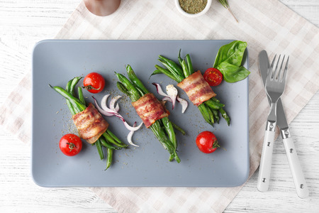 Plate with delicious bacon-wrapped green beans on table