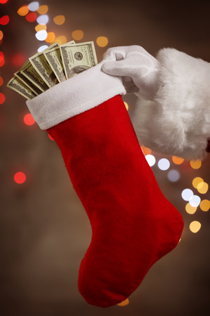 Santa Claus holding stocking with money against defocused lightsの写真素材
