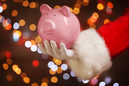 Santa Claus holding piggy bank against defocused lightsの写真素材