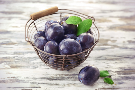 Metal basket with ripe plums on tableの写真素材