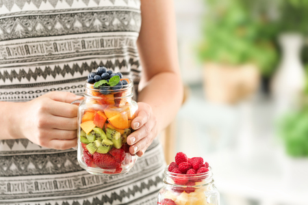 Woman holding mason jar with fruits and berries on blurred backgroundの写真素材