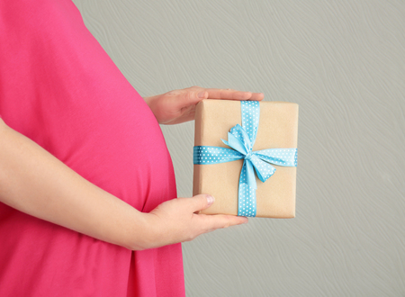 Pregnant woman holding baby shower gift against color backgroundの写真素材