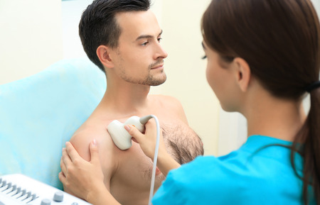 Doctor conducting ultrasound examination of patient's shoulder in clinicの写真素材
