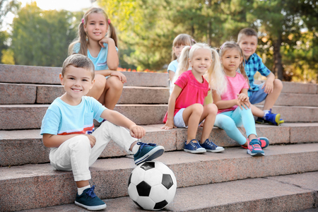 Cute little children with ball sitting on stairs in city parkの写真素材