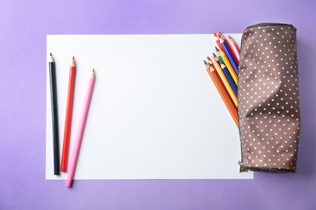 Blank sheet of paper and color pencils on violet background