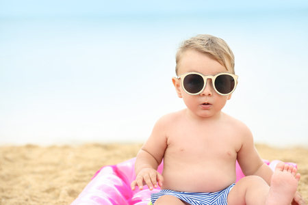 Cute baby boy sitting on inflatable mattress at beachの写真素材