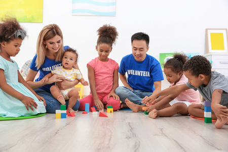 Young volunteers playing with little children in light room. Volunteering abroad conceptの写真素材