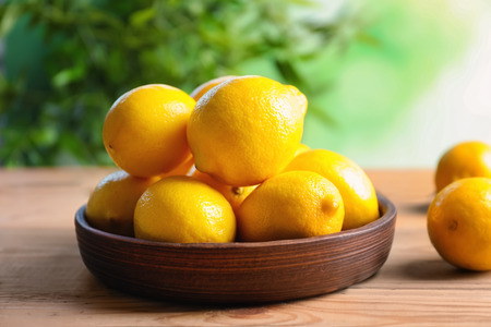 Wooden plate with ripe lemons on table against blurred backgroundの写真素材