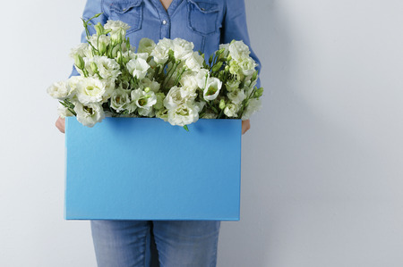 Woman holding paper box with beautiful flowers against white wallの写真素材