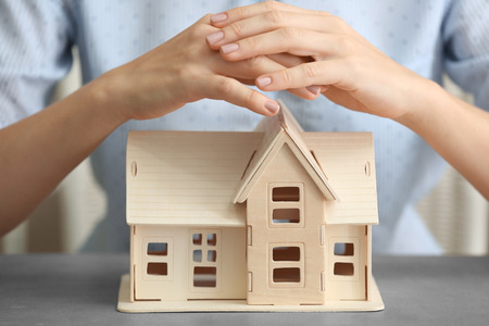 Woman holding hands over wooden house at table, close upの写真素材
