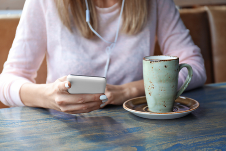 Beautiful young woman with mobile phone listening to music in cafeの写真素材