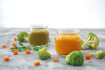 Jars with baby food on table against white backgroundの写真素材