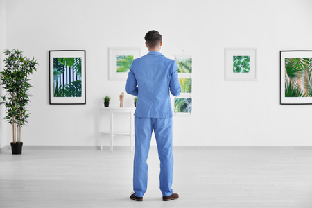 Young man looking at picture of tropical foliage in art galleryの写真素材