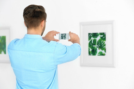 Young man taking photo of picture in art gallery