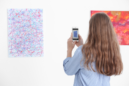Young woman taking picture of painting in art galleryの写真素材