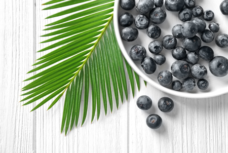 Plate with fresh acai berries and palm leaf on wooden tableの写真素材