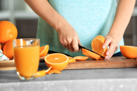 Woman cutting orange on board in kitchenの写真素材