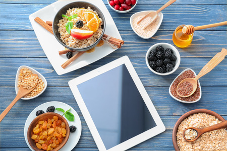 Composition of tasty oatmeal with fruits and tablet on wooden backgroundの写真素材