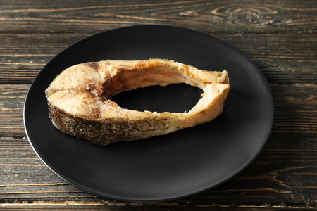Black plate with fried fish steak on wooden background