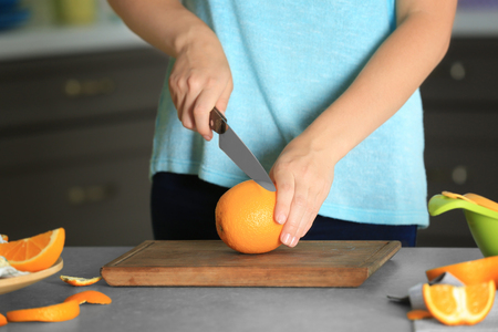 Woman cutting orange on board in kitchenの写真素材