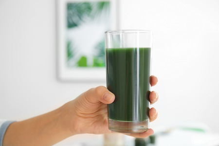 Woman holding glass with spirulina drink indoorsの写真素材