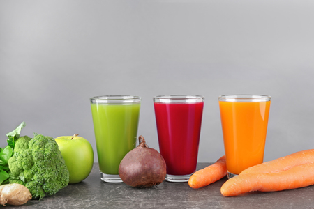 Glasses with various fresh juices and ingredients on tableの写真素材