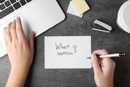 Woman writing "What is autism?" on sheet of paper at tableの写真素材