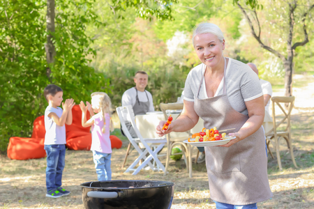 Mature woman cooking vegetables on barbecue grill outdoorsの写真素材
