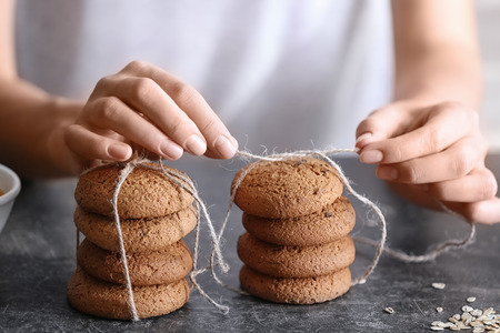 Woman tying delicious oatmeal cookies with rope on kitchen table, closeupの写真素材