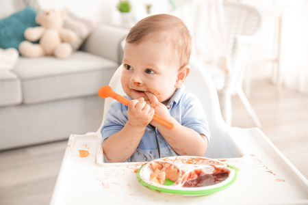 Cute messy baby eating puree at homeの写真素材