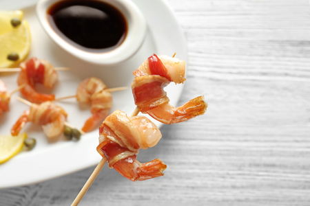 Bacon-wrapped shrimps on skewer over plate, closeupの写真素材