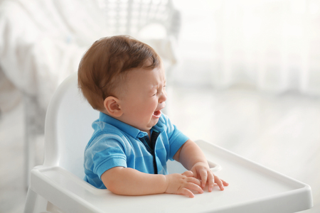 Cute little crying baby sitting on chair indoorsの写真素材