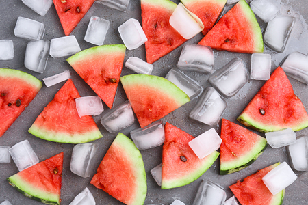 Slices of ripe watermelon and ice cubes on gray background