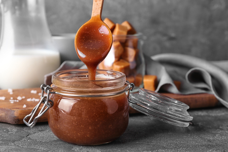 Spoon with tasty caramel sauce over jar on tableの写真素材