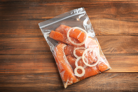 Marinated slices of salmon fillet in plastic bag on wooden backgroundの写真素材