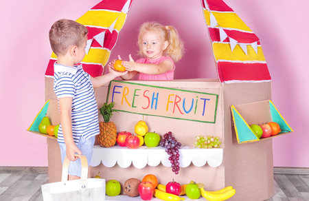 Little children playing with cardboard stall on color wall backgroundの写真素材