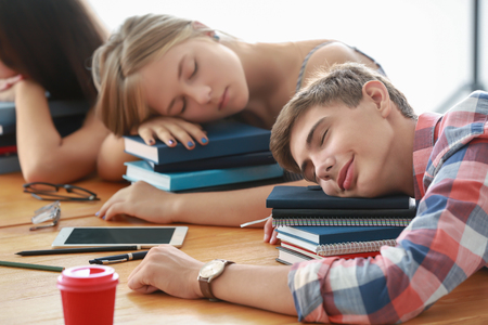 Tired students sleeping at tableの写真素材