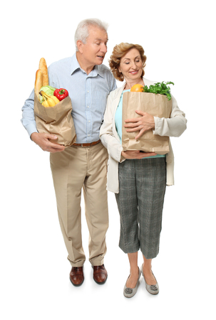 Elderly couple holding paper bags with groceries on white backgroundの写真素材
