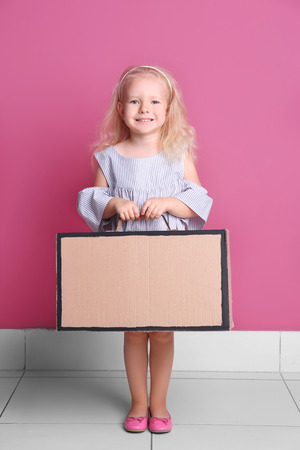 Little girl playing with cardboard suitcase on color wall backgroundの写真素材
