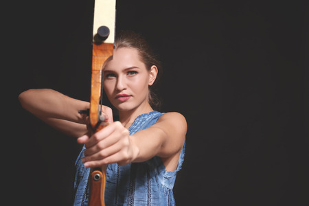 Young woman practicing archery on dark background
