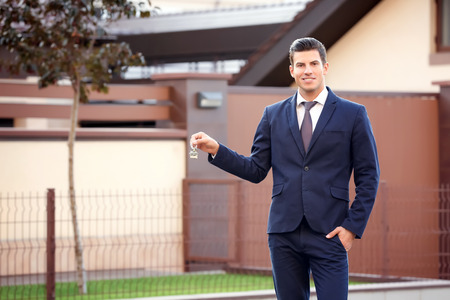 Male real estate agent holding key near houseの写真素材