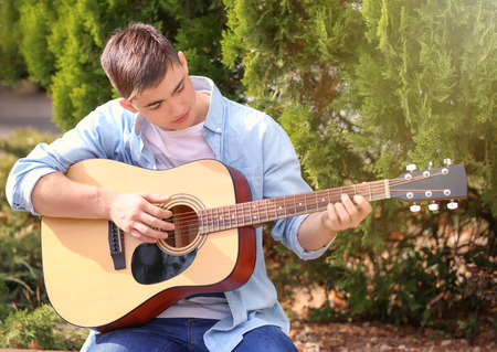 Talented teenager playing acoustic guitar in park