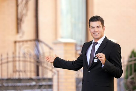 Male real estate agent holding key near houseの写真素材