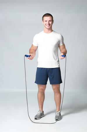 Young man with jumping rope on light backgroundの写真素材