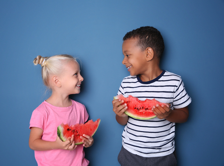 Cute kids eating watermelon on color backgroundの写真素材