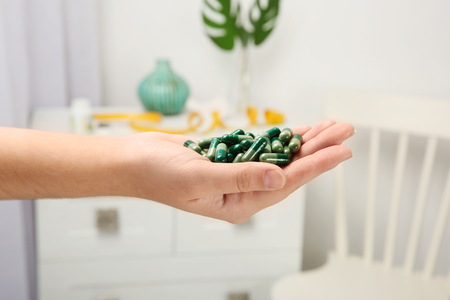 Woman holding spirulina capsules indoors, closeupの写真素材